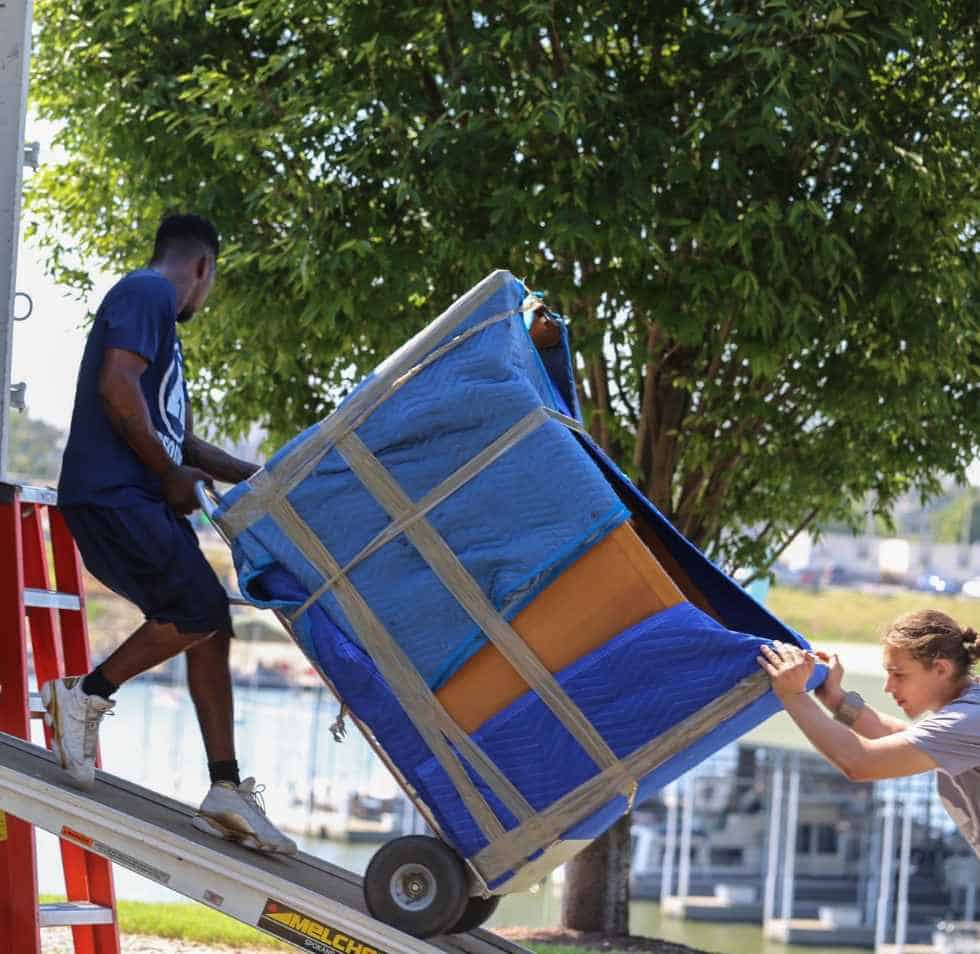 Two Absolute crew members roll a piece of furniture wrapped in moving blankets and bands up the truck ramp